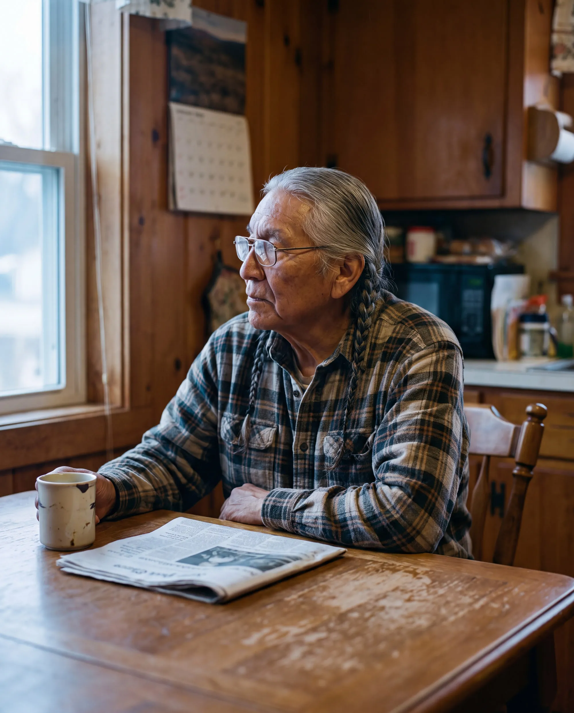 A retired man with a newspaper and coffee at his kitchen table in the morning.